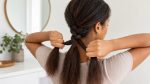 Woman separating three hair sections while braiding her own hair