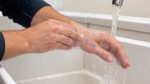 Hands gently washing small blue paint spots with soap and running water